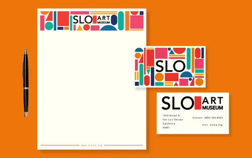Art museum letterhead and business cards with colorful geometric borders, arranged with a black pen on an orange background.